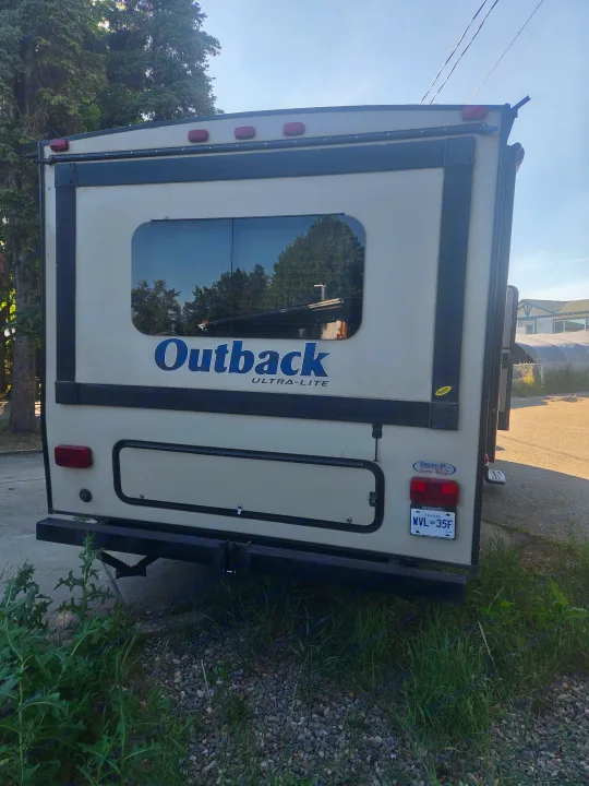 Rear view of an Outback ULTRA-LITE travel trailer (rv rental). Features a window, storage compartment, brake lights, and license plate WVL 35F.. Keystone Outback 2017