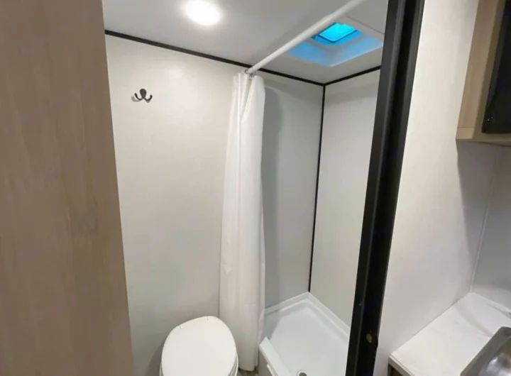 Efficient RV rental bathroom with toilet, shower, and skylight. This compact space features hooks and bright lighting.. 4YDTCME14TM932345 13B 2025