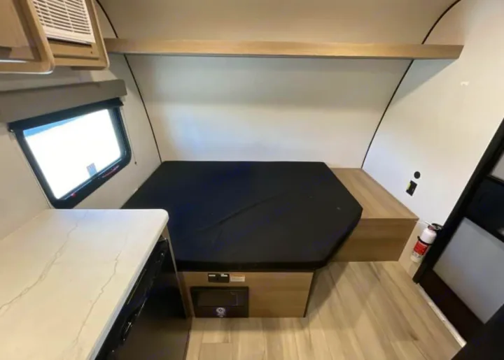 Compact rv rental interior with a hexagonal bed, small counter, window, and fire extinguisher for safety.. 4YDTCME14TM932345 13B 2025