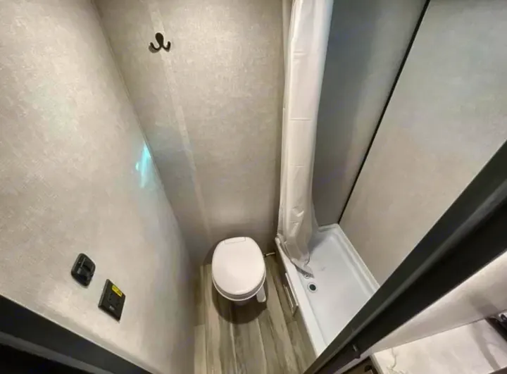 Compact RV rental bathroom featuring a toilet, shower stall with curtain, and a wall hook.. 4YDTCME14TM932345 13B 2025