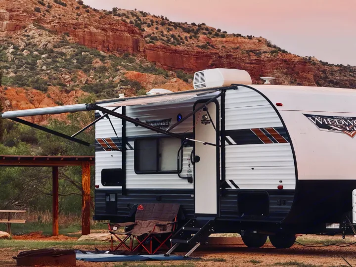 RV rental: A travel trailer with an extended awning set up at a beautiful campsite against red rock mountains at dusk.. Forest River Wildwood X-Lite 2021