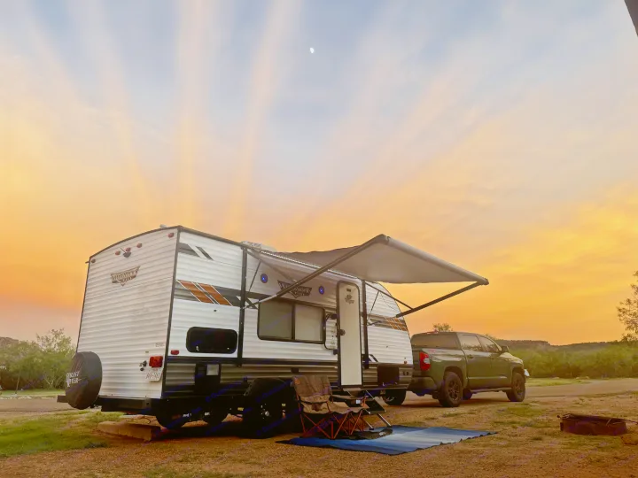 RV rental camping setup with truck and chairs under a vibrant sunset sky, a crescent moon visible.. Forest River Wildwood X-Lite 2021