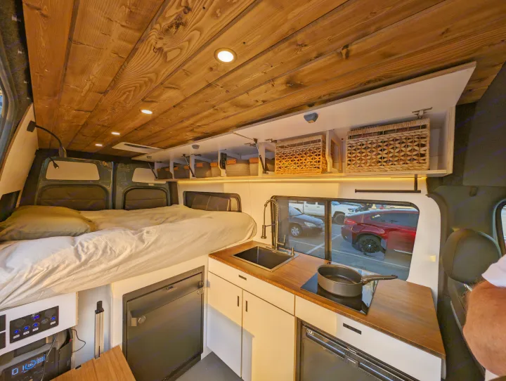 Modern rv rental interior showing a comfortable bed, compact kitchen with sink & stove, and overhead storage.. Mercedes-Benz Sprinter 2023