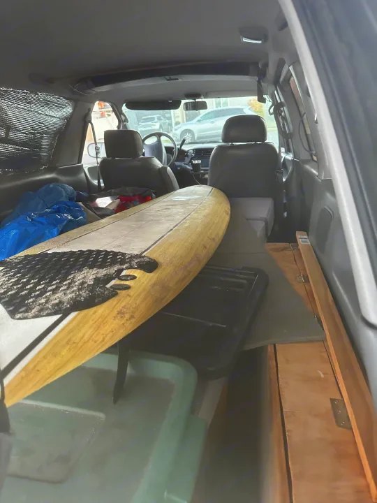 Inside an RV rental: a surfboard and camp gear on a custom wood platform, ready for van life and road trip adventures.. Toyota Previa 1996