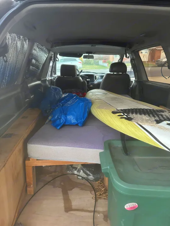 Van interior converted for camping: bed, surfboard, bags, and storage bin. Ready for a road trip or practical rv rental use.. Toyota Previa 1996
