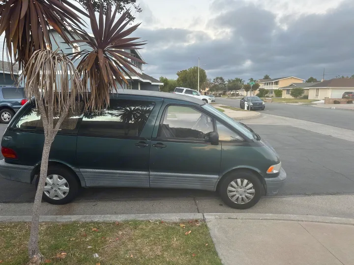 Dark green minivan parked on a residential street. A compact travel vehicle, different from a spacious rv rental.. Toyota Previa 1996
