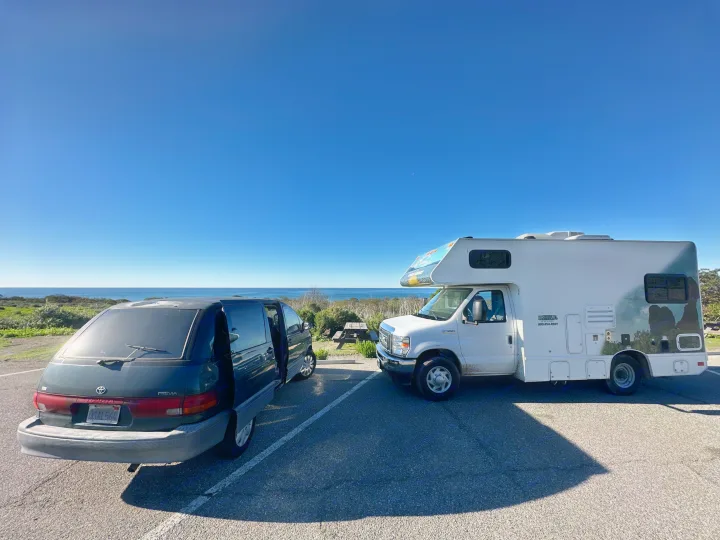 Cruise America RV rental and Toyota minivan parked by the ocean under a clear blue sky with a crescent moon.. Toyota Previa 1996