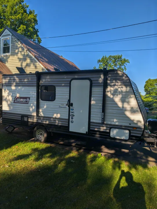 Coleman Dutchmen travel trailer, an RV rental option, parked outside a house with sun and tree shadows.. Dutchmen Coleman Lantern LT 2021