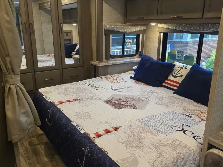 Cozy RV rental bedroom with a nautical-themed quilt, blue pillows, and mirrored closet. Ideal for travel adventures.. Thor Four Winds 2023