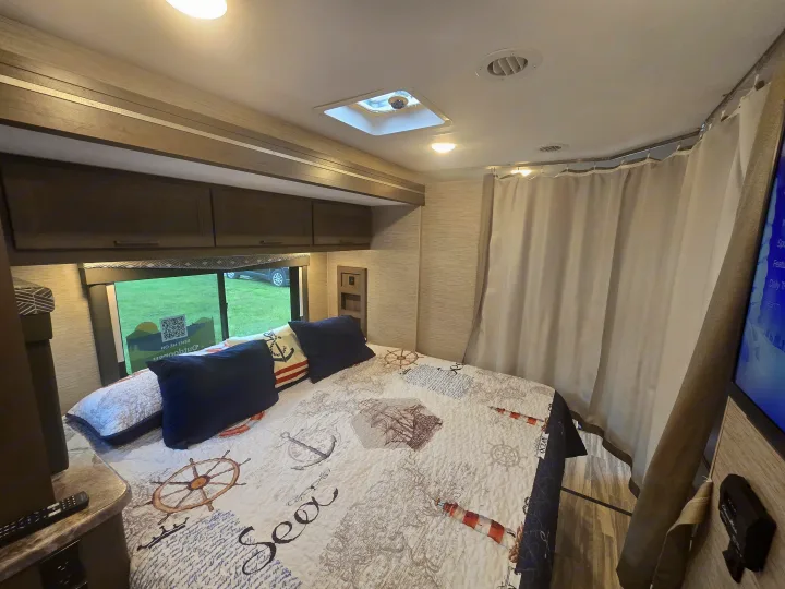 Inside a cozy RV rental bedroom: nautical bedding, overhead storage, and a bright skylight.. Thor Four Winds 2023