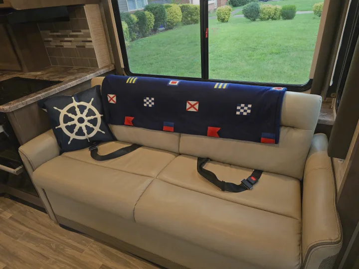 RV rental living area with a light sofa, seatbelts, nautical decor, kitchen, and green outdoor view.. Thor Four Winds 2023
