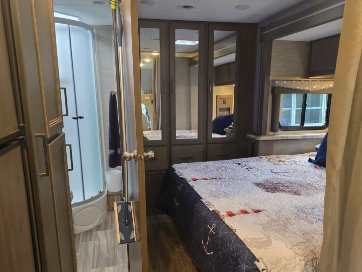 Inside this cozy RV rental: a compact shower, comfy bed with a nautical quilt, and mirrored storage, designed for road trips.. Thor Four Winds 2023