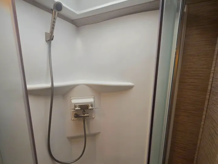 Clean RV rental shower stall with handheld showerhead and controls, perfect for travel and camping.. Thor Four Winds 2023