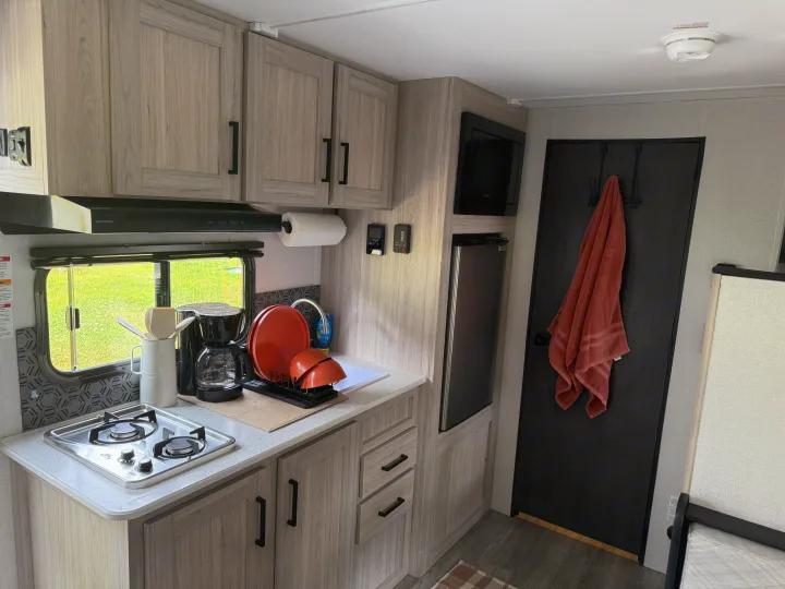 Experience your RV rental's compact kitchen, featuring a two-burner stove, sink, coffee maker, microwave, and fridge.. Heartland's RV Mallard 17 BHL 2025