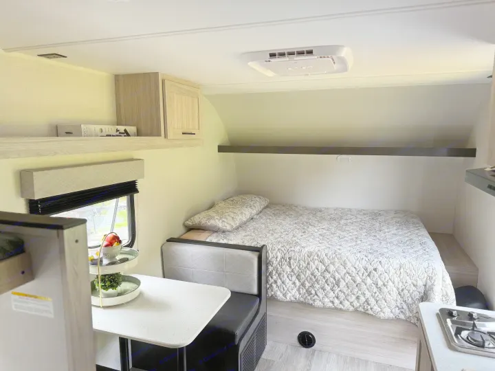 Cozy RV rental interior with bed, dinette, kitchenette, and overhead storage. Features light wood tones and a window view.. Heartland's RV Mallard 17 BHL 2025