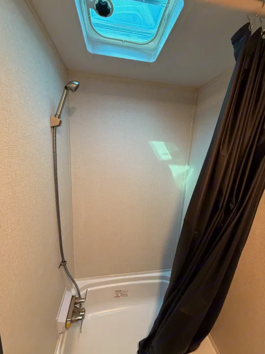 Inside an RV rental, a compact shower and tub combo features a handheld showerhead, dark curtain, and ceiling skylight.. Heartland's RV Mallard 17 BHL 2025