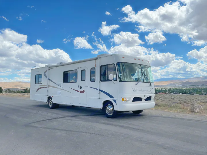 This RV rental awaits new adventures on a scenic overlook, featuring a wide view of mountains under a cloudy sky.. Four Winds Hurricane 2000