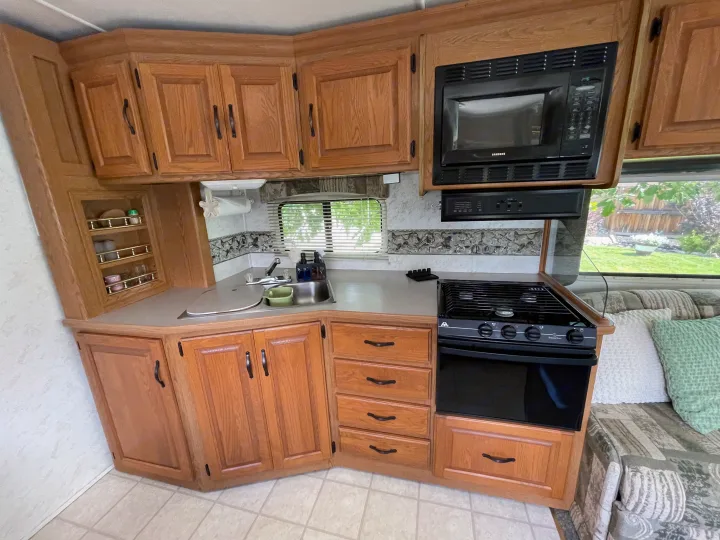 An RV rental's well-equipped kitchen featuring wooden cabinetry, a sink, microwave, stove, and convenient storage options.. Four Winds Hurricane 2000