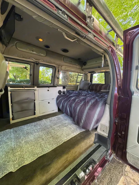 View inside an RV rental van's living area: striped bed, counter with sink, storage, and a floor rug.. Chevrolet Open Road 2005