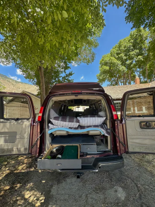 Converted van's rear open, showing a cozy bed and pull-out camp kitchen. A perfect rv rental for outdoor adventures.. Chevrolet Open Road 2005