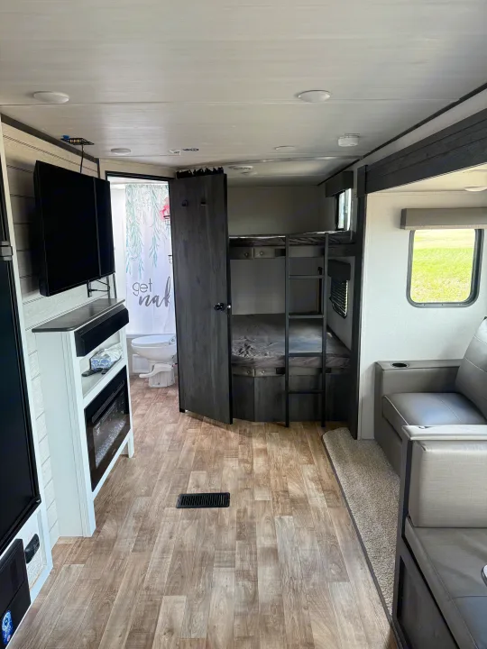 Step inside this RV rental, showcasing bunk beds, a sofa, TV, and a bathroom. A cozy camper interior with wood-look floors.. Keystone RV Hideout 2023