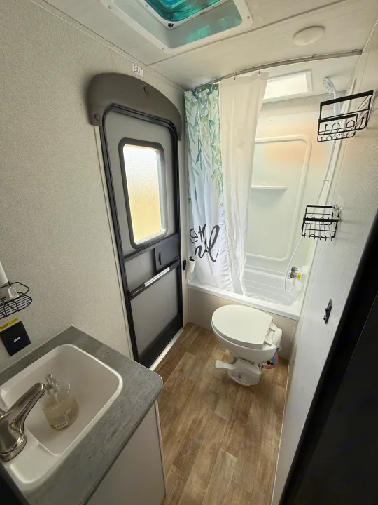 RV rental bathroom: sink, toilet, shower/tub, & an 'EXIT' labeled door. A bright, functional space with wood-look floor.. Keystone RV Hideout 2023