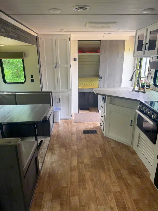 Modern RV rental interior featuring a bright kitchen, dinette, and glimpse into the bunk bed area, with wood-look flooring.. Keystone RV Hideout 2023