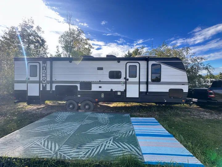 A white and black Keystone Hideout travel trailer rv rental with outdoor rugs, ready for a serene camping getaway.. Keystone RV Hideout 2023