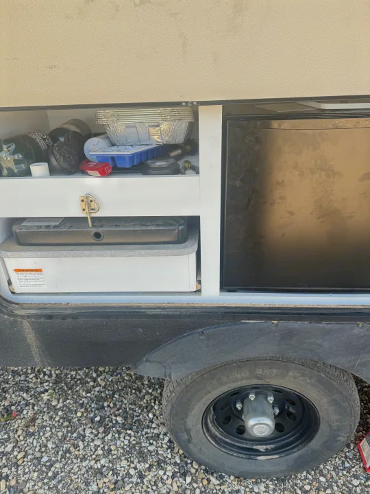 RV rental exterior storage: organized compartment with a mini fridge, camping stove, and essential outdoor kitchen supplies.. Keystone RV Hideout 2023
