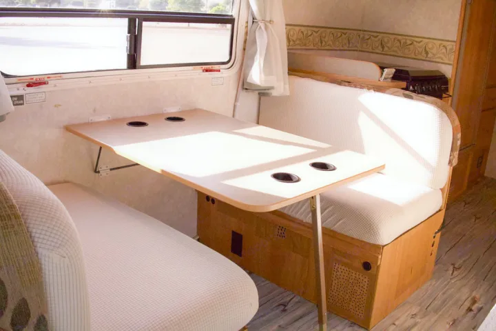 Bright RV rental dinette with a folding table, built-in cup holders, comfy benches, and a large window, ready for travel.. R-Vision Trail-Lite 2002