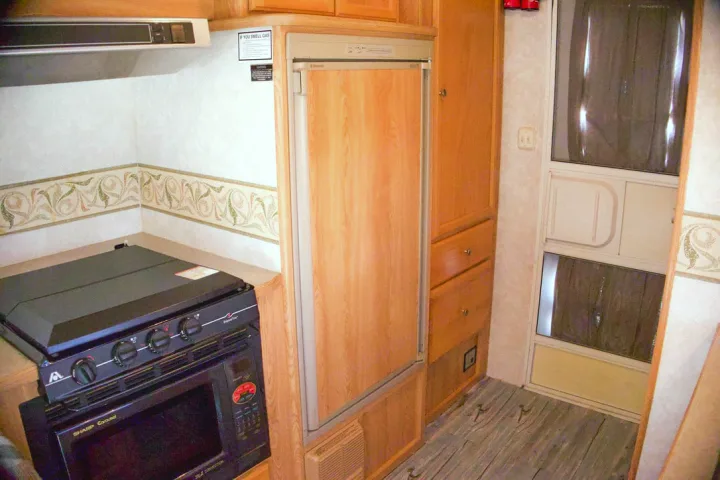 Inside an RV rental: a practical kitchen with a gas stove, microwave, refrigerator, and cabinetry for trips.. R-Vision Trail-Lite 2002