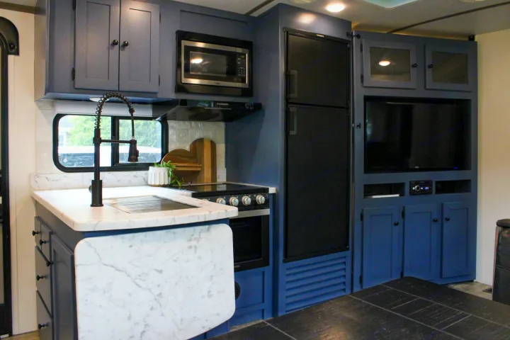 Renovated RV rental interior with stylish blue kitchen cabinets, marble-look counters, and a modern entertainment center.. Keystone RV Outback Ultra-Lite 2021