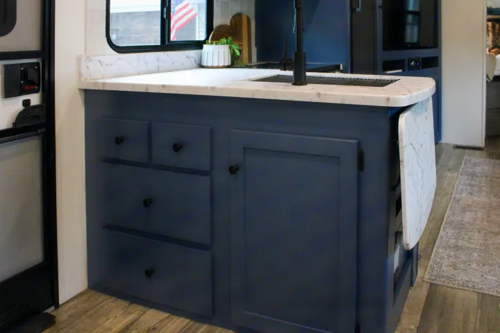Stylish RV rental interior: blue cabinets, marble-look counter with sink, and a space-saving fold-down table.. Keystone RV Outback Ultra-Lite 2021