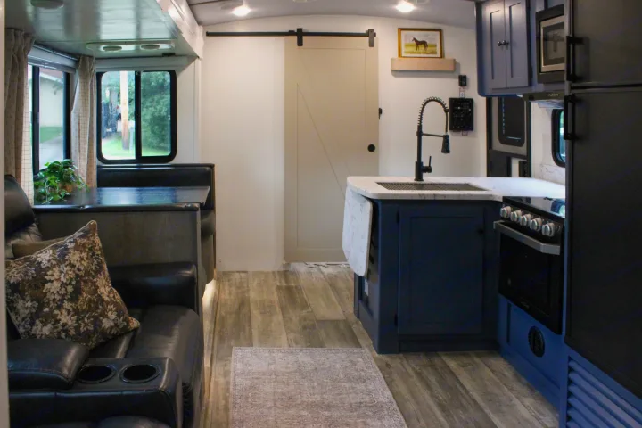 This rv rental features a renovated interior with a cozy seating area, modern kitchen with blue cabinets, and wood-look floors.. Keystone RV Outback Ultra-Lite 2021