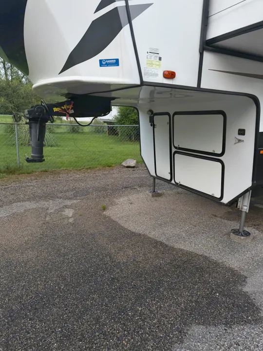 Front of a white fifth-wheel RV rental, featuring its hitch, storage, and landing gear, parked on a paved lot.. Heartland RVs Bighorn Traveler 2022