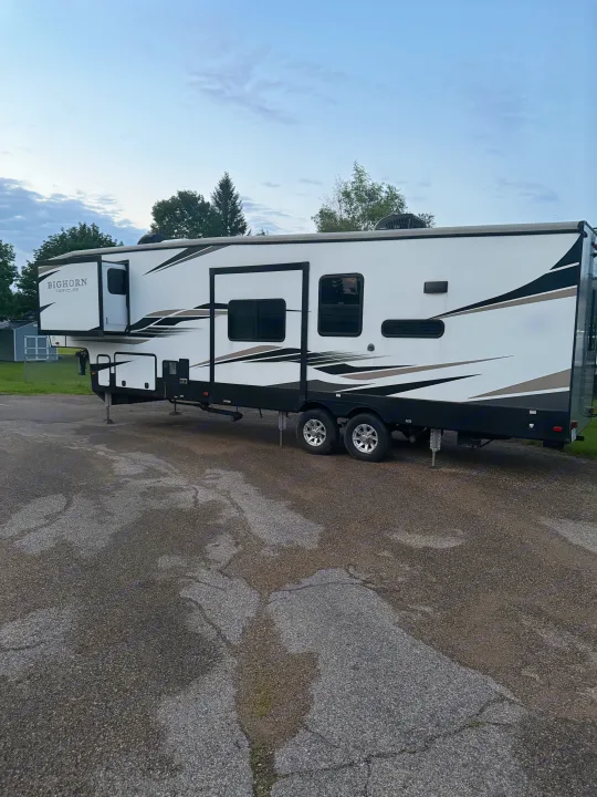 A white Bighorn Traveler fifth-wheel RV rental with black and tan graphics, parked on asphalt with slide-outs extended.. Heartland RVs Bighorn Traveler 2022