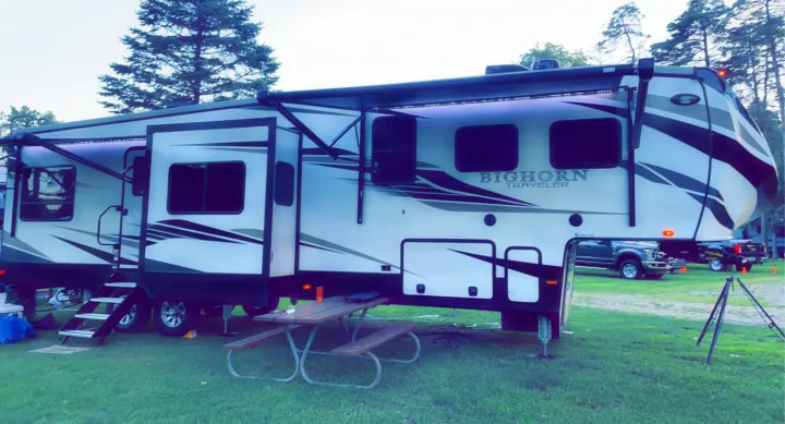 White Bighorn Traveler fifth-wheel rv rental with extended awning & picnic table, fully set up for camping on green grass.. Heartland RVs Bighorn Traveler 2022