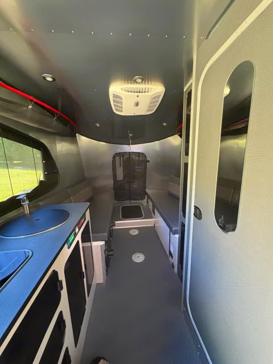Modern RV rental interior with gray walls, hexagonal floor, kitchenette, bench seating, and overhead AC unit.. Airstream Basecamp 2025
