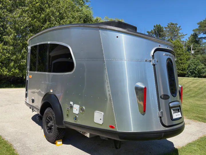 A compact, shiny silver Airstream Basecamp travel trailer, seen from the rear, perfect for an RV rental camping trip.. Airstream Basecamp 2025