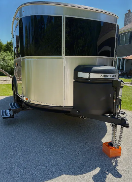 An Airstream travel trailer, ready for an RV rental, parked on pavement with its hitch on orange blocks and steps extended.. Airstream Basecamp 2025