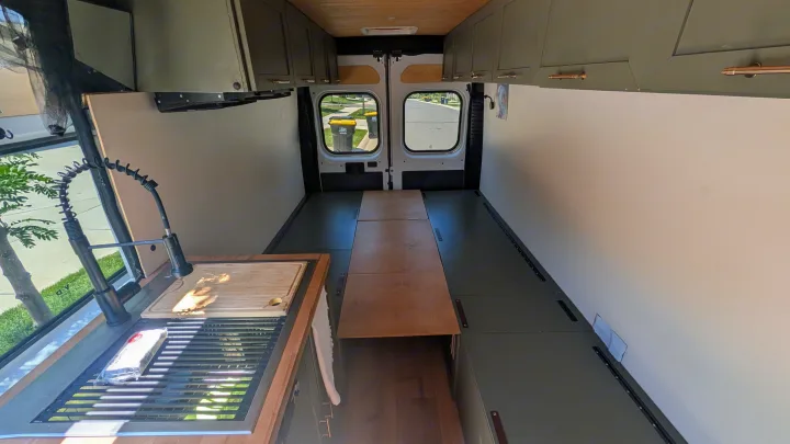 This RV rental's interior reveals a modern van conversion with a kitchen sink, overhead cabinets, and a convertible bed/table.. Dodge Ram 1500 2022