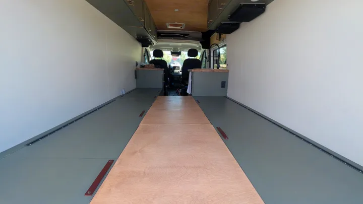 Spacious RV rental interior featuring a grey floor with wooden center, white walls, and overhead cabinets, looking toward the front cabin.. Dodge Ram 1500 2022