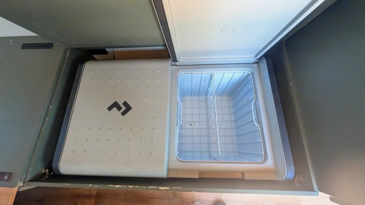 RV rental: An open, empty portable fridge with a wire basket, nestled in a dark green cabinet.. Dodge Ram 1500 2022