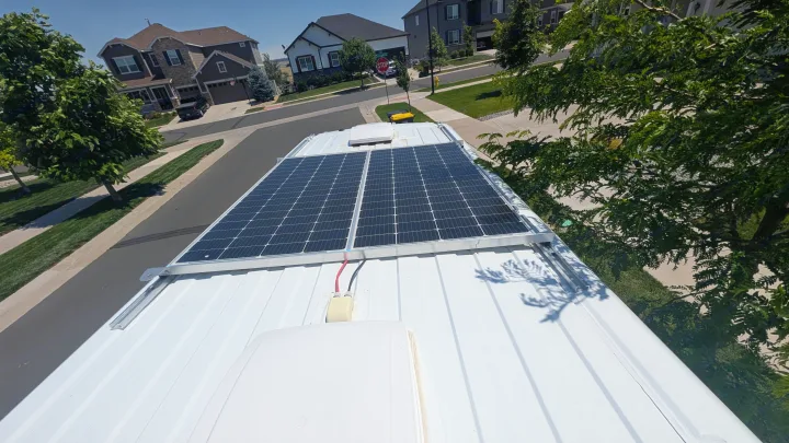 Top-down view of an RV rental with two solar panels on its white roof, providing off-grid power in a sunny suburban neighborhood.. Dodge Ram 1500 2022