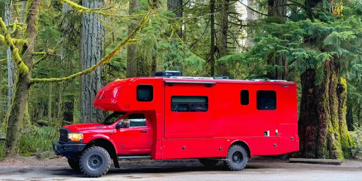 Bright red off-road rv rental, a rugged camper truck, parked amidst moss-covered trees in a lush forest, perfect for adventure.. Dynamax ISATA 5 Explorer Extreme Package 2026
