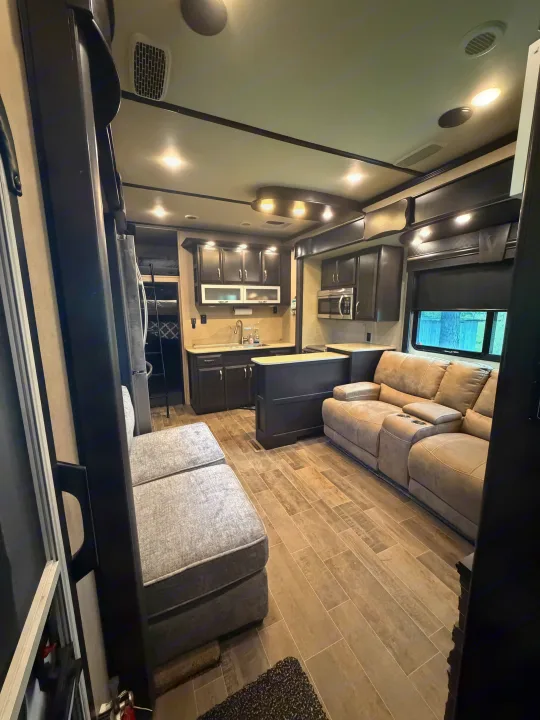 Spacious RV rental interior with kitchen, living area, and bunk beds. Features wood-look flooring and modern dark cabinetry.. Denali Denali Fifth Wheel 2017