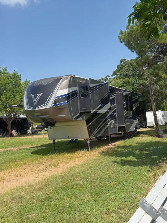 This gray fifth-wheel RV rental is parked with its slide-outs extended on a grassy lot under a clear sky.. Denali Denali Fifth Wheel 2017