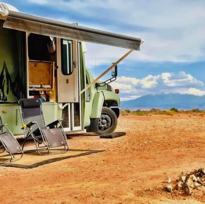Your next RV rental adventure! Green campervan under an awning with chairs, set against desert mountains.. Chevy C4500 Kodiak 2008