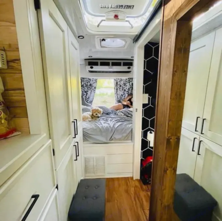 This cozy RV rental features a compact bedroom with a person and dog on the bed, smart storage, and seating.. Chevy C4500 Kodiak 2008