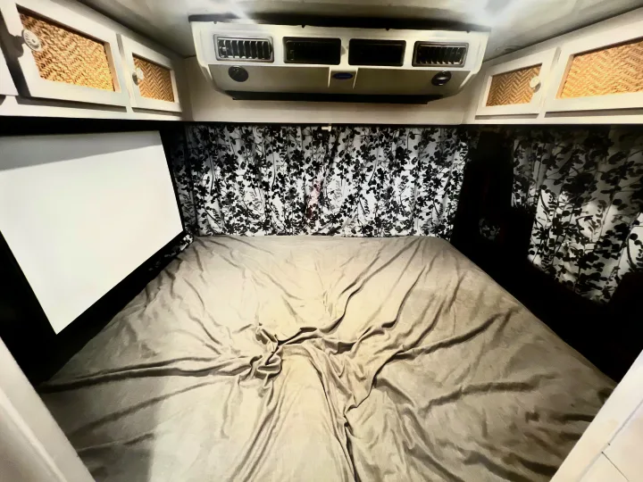 Cozy RV rental bedroom: bed, patterned curtains, woven cabinets, AC unit, and a handy projector screen.. Chevy C4500 Kodiak 2008